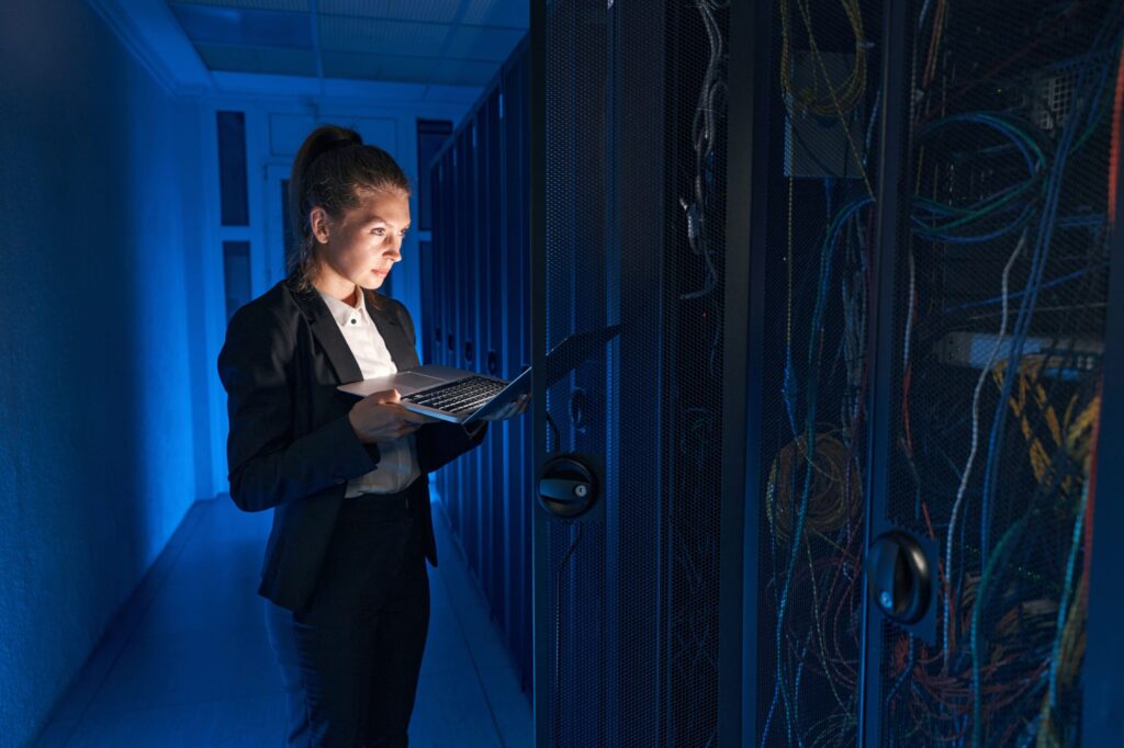 woman looking at her laptop computer while standing in a data center hallway